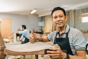 Carpenter working with electric planer on wooden plank in workshop. Craftsman makes own successful small business, Asian man using tool in carpenter's shop to making a furniture from wood - obrazy, fototapety, plakaty