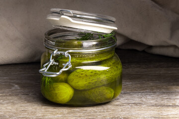 A glass home canning jar of baby dill pickles with the lid open