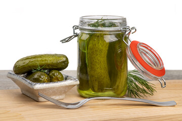 A glass home canning jar of baby dill pickles with the lid open and pickles on a small plate...