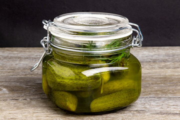A glass home canning jar of home made baby dill pickles on a dark wooden pantry shelf