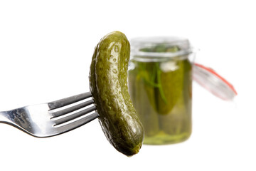 A dill pickle on a fork with a glass home canning jar of pickles out of focus in the background...