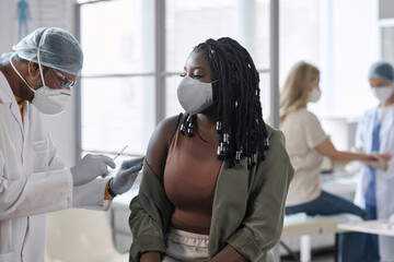 Portrait of young Black woman wearing mask getting vaccination shot in clinic copy space