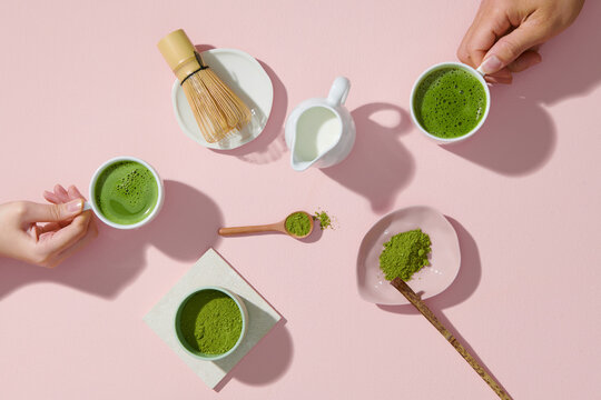 hand hold Matcha latte in a cup, powder and tools for making tea