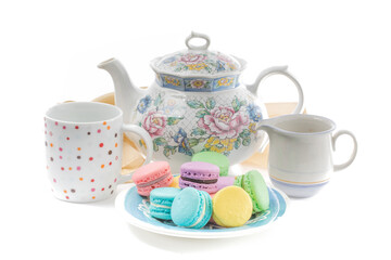 a plate of colorful meringue or  macaron cookies and a teapot and cup on a white background
