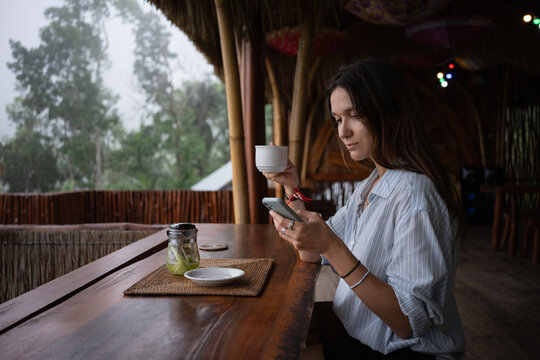 Woman Sitting at Table Using Cell Phone in Forest Cafe
