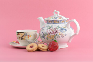 strawberry cream cookies and strawberries and a colorful teapot and teacup on a pink background