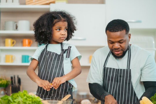 In a home kitchen, black father and his daughter bond over cooking a meal food, their laughter and love filling the air, embodying the joy of African American family life, Father's Day concept