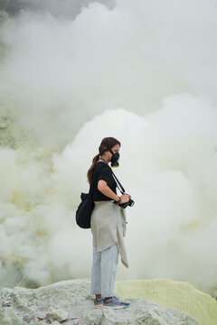 Traveller wearing respirator stands in volcano crater with sulfur gas