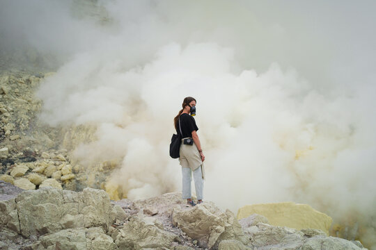 Traveller wearing respirator stands in volcano crater with sulfur gas