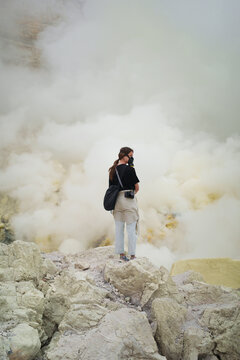 Traveller wearing respirator stands in volcano crater with sulfur gas