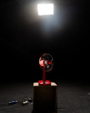 A red fan sitting on a wooden box with a studio light pointed at it