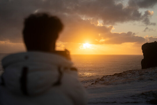 A photographer faces the sea in Iceland before sunset in winter.