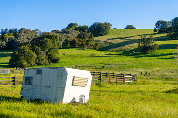 Camper parked on farmland with large tree and green rolling hills