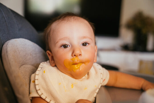 Cute baby with messy mouth sitting on chair in living room