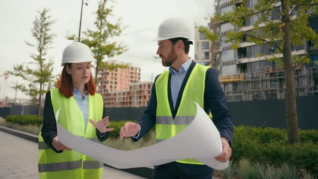 Two contractors civil engineers discuss electrical maintenance blueprint paper partnership discuss teamwork city buildings project construction builders woman man architects plan urban development