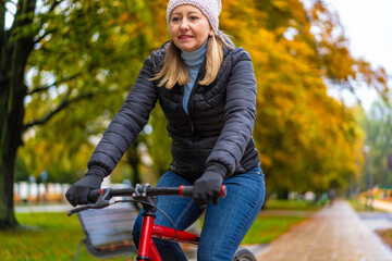 Mid-adult woman riding bicycle in city park on a rainy day
