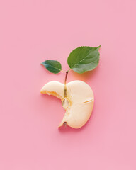 Bitten cookie designed as apple core with green leaves isolated on pastel pink background. Minimal concept of natural sweet food, wellness, temptation, sin. Flat lay, top view.