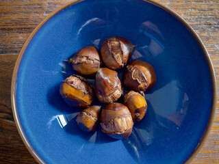 Eight brown toasted chestnuts in a blue ceramic bowl on a rustic wooden teak table