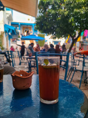 Close-up view of a cup of tea on a cafe terrace table in Sidi Bou Said, a famous village with traditional white and blue Tunisian architecture and flowering plants. Tunisia.