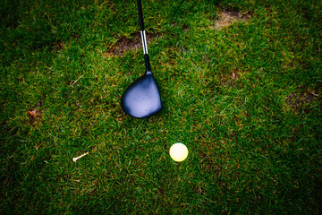 Close-up of a golf club about to hit a yellow golf ball on grass...