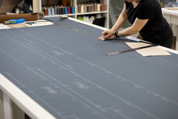 A professional dressmaker marks out the fabric for the pattern using a long metal ruler. Female...