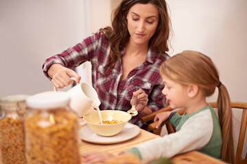 Mother, girl and breakfast in house with cereal for health, nutrition and help by table. Woman, kid and brunch together in home with milk by kitchen for wellness, eating and assistance with food