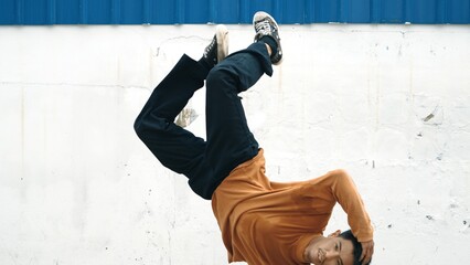 Hispanic man stretch arms and dance break dancing in front of wall. Motion shot of stylish street...