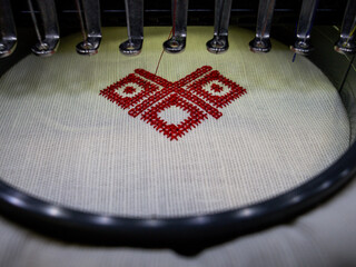 Machine embroidery of a cross-stitch ornament. Red thread ornament embroidery on white fabric.