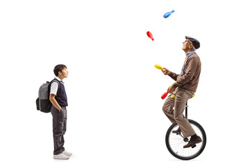 Boy standing and watching an elderly man riding a mono cycle and juggling