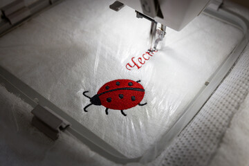 Machine embroidery of red ladybug and text on white towel. Ladybug embroidery.
