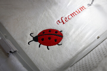 Machine embroidery of red ladybug and text on white towel. Ladybug embroidery.