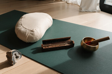 Closeup shot of a yoga mat with incense bar, meditation cushion and singing bowl, preparation for sound healing relaxation ritual practice at home. 