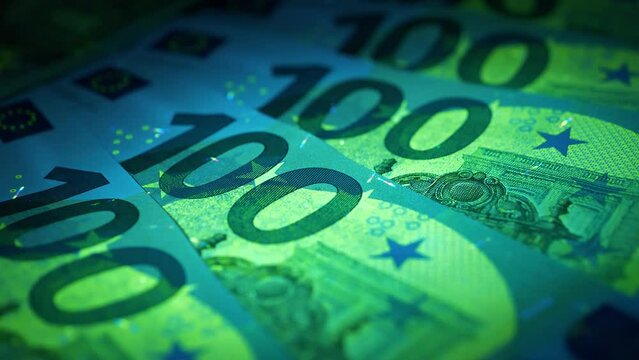 Security signs and elements on euro banknotes glow under ultraviolet light. Green and blue 100 Euro banknotes under UV light