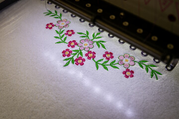 Machine embroidery of beautiful flowers on white towel. Embroidery of pink flowers with green leaves. Top view.