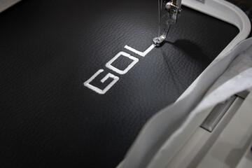 Machine embroidery of text with white thread on black leather. Embroidery on auto cushion.