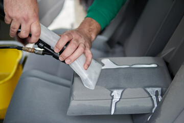 Car cleaning detailing - male using professional steam vacuum chemical cleaning for dirty car...