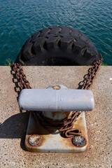 Seafaring: Gray bollard with a large chained old tractor tire as a fender in a ferry port