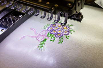 Machine embroidery of a bouquet of flowers on white towel. Embroidery of a bouquet of purple flowers with a purple ribbon.