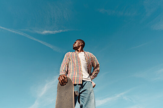 Black man with skateboard in blue sky with copyspace