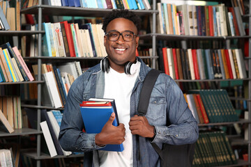 Happy male buyer chose interesting books in bookstore, happy with purchase. Portrait of smiling african college student with headphones around his neck, holding a stack of books. 