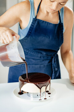 Pastry chef pours chocolate icing on mousse cake