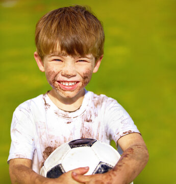 Portrait, smile and child with football outdoor for sports, exercise or game at garden in summer. Face, boy and happy kid with soccer ball at park with mud, messy or dirty for recreation in Sweden