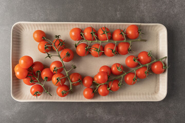 Small tomatoes in a plate on a gray background. Cherry tomatoes on a sprig. - Powered by Adobe