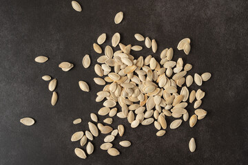 Pumpkin seeds are scattered on the table. White pumpkin seeds on a dark background, close-up.