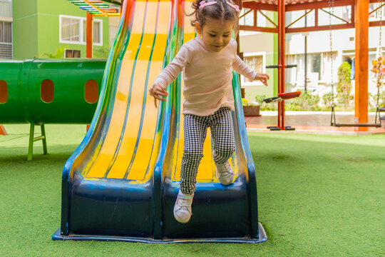 Una linda ni&ntilde;a de dos a&ntilde;os sonriente juega en un tobogan dentro del patio de un condominio.