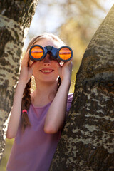 Tree, girl and binoculars for safari, search and looking for animals on travel holiday. Smile, fun and seek for bird watching or wildlife in nature, happy young child and scenery or view in Kenya