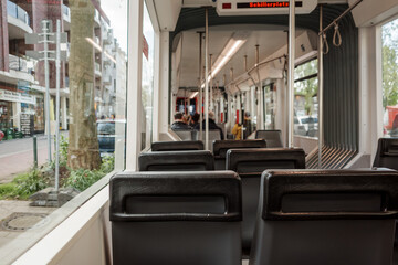 The interior of a city tram showing empty leather seats with the tram in motion, the sign...