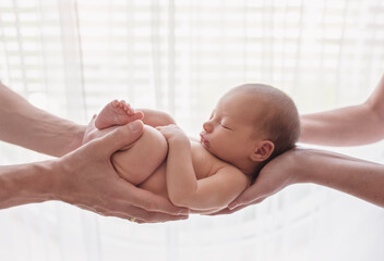 Tiny sleeping newborn baby in his mother's and father's hands. 