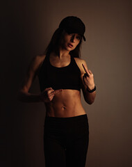 Fuck you. Sport sexy muscular woman posing in black sport bra, cap and showing the fuck sign the hand, standing on dark shadow studio background. Front body view.