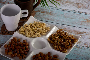 Assorted nuts are laid out on a square-shaped plate along with empty glasses for hot drinks. Dried nuts of various types are beautifully placed on a square saucer standing on a wooden table